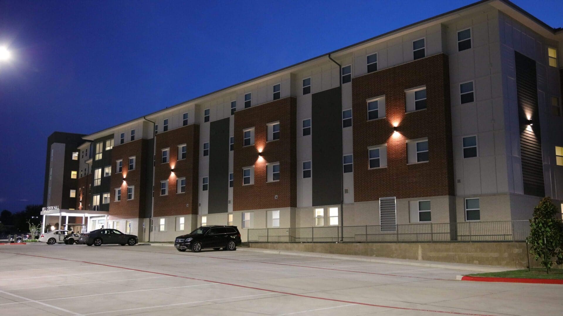 A parked black car outside a modern apartment building at dusk.