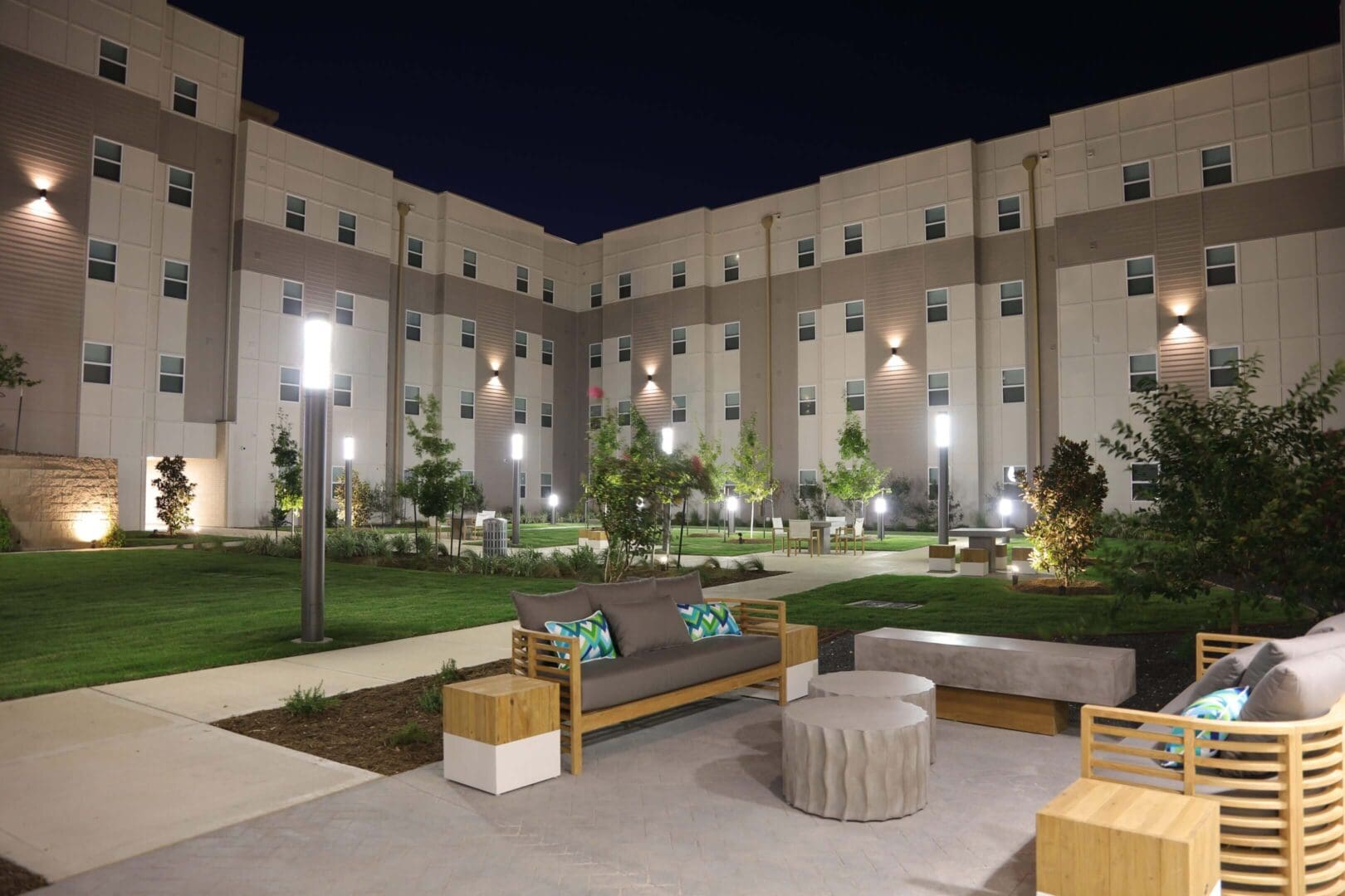 Well-lit courtyard with benches and greenery at night.