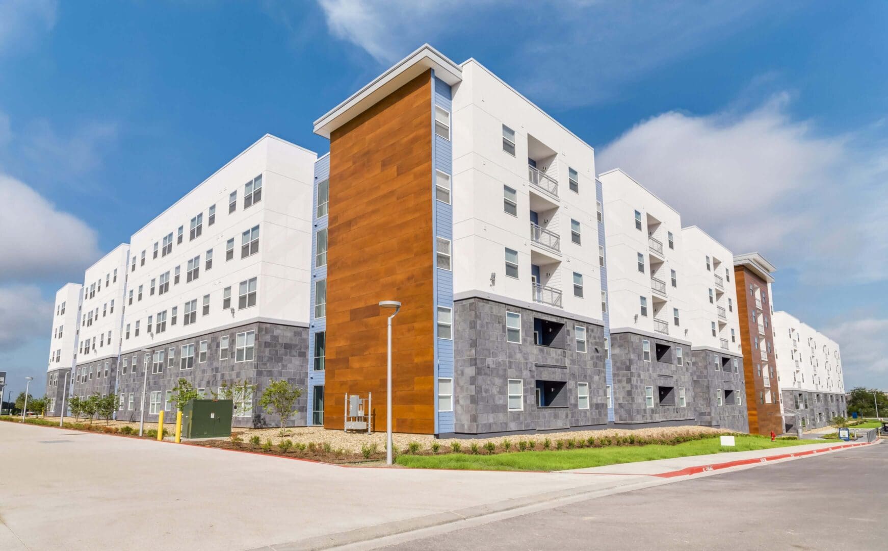 Modern multi-story apartment building with white and wood-paneled exterior under a blue sky.