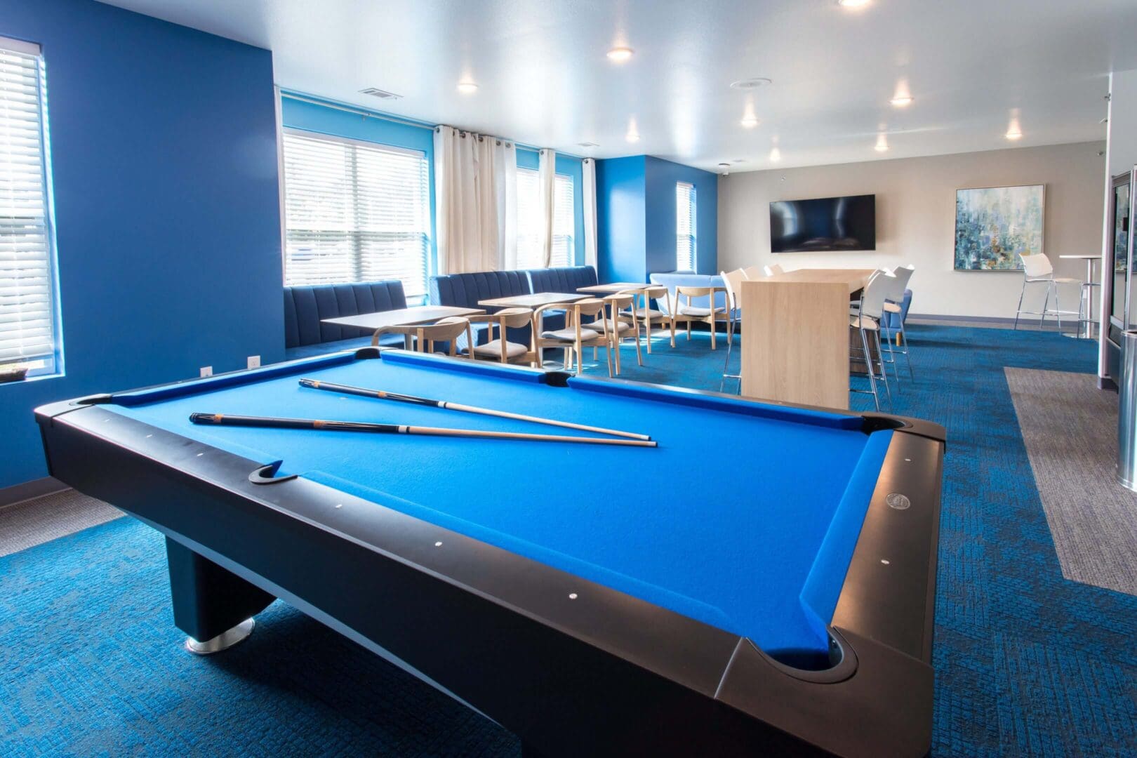 Modern billiards room with blue felt pool tables and seating area.