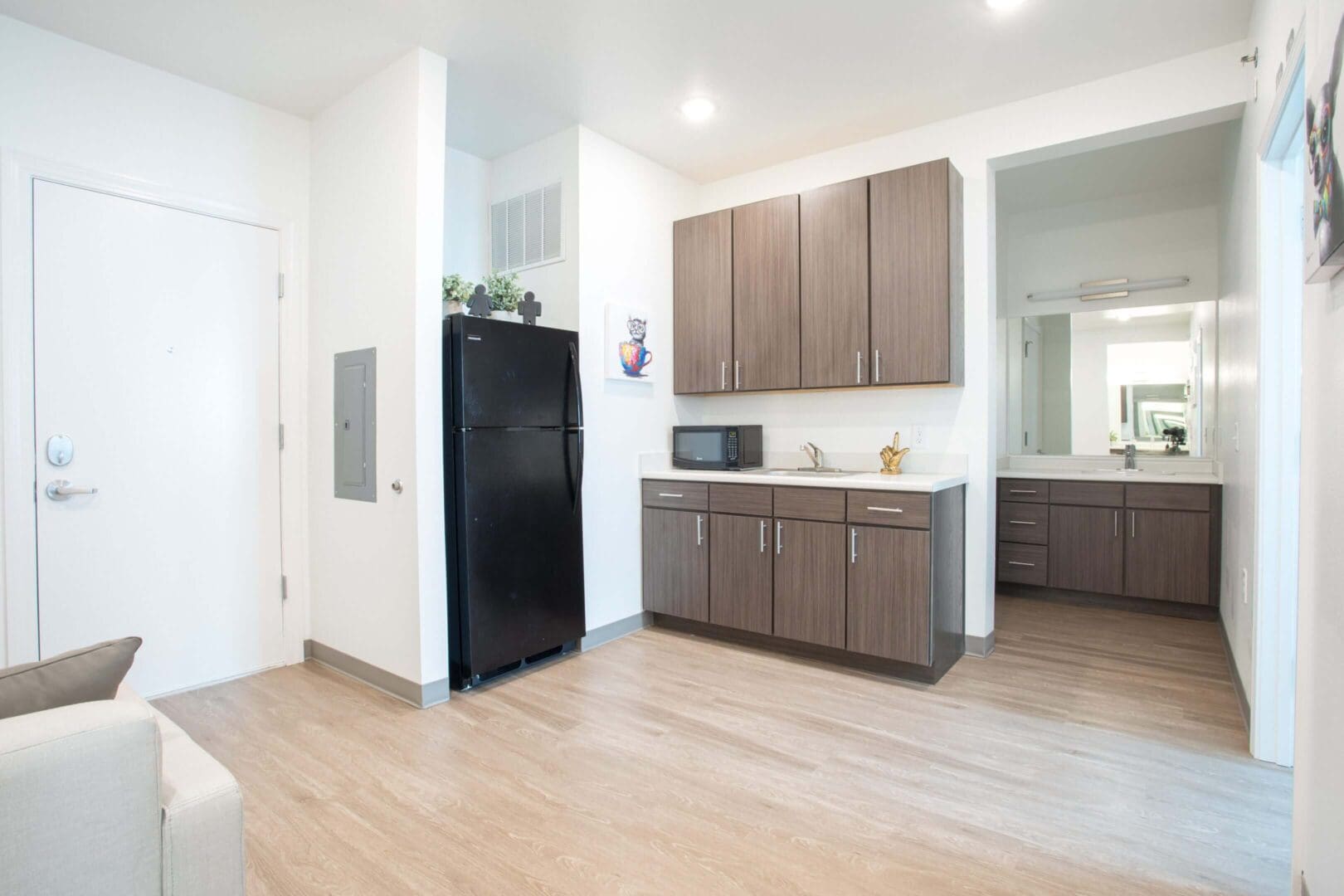 Bright kitchen with wooden cabinets and black refrigerator on light wood floors.